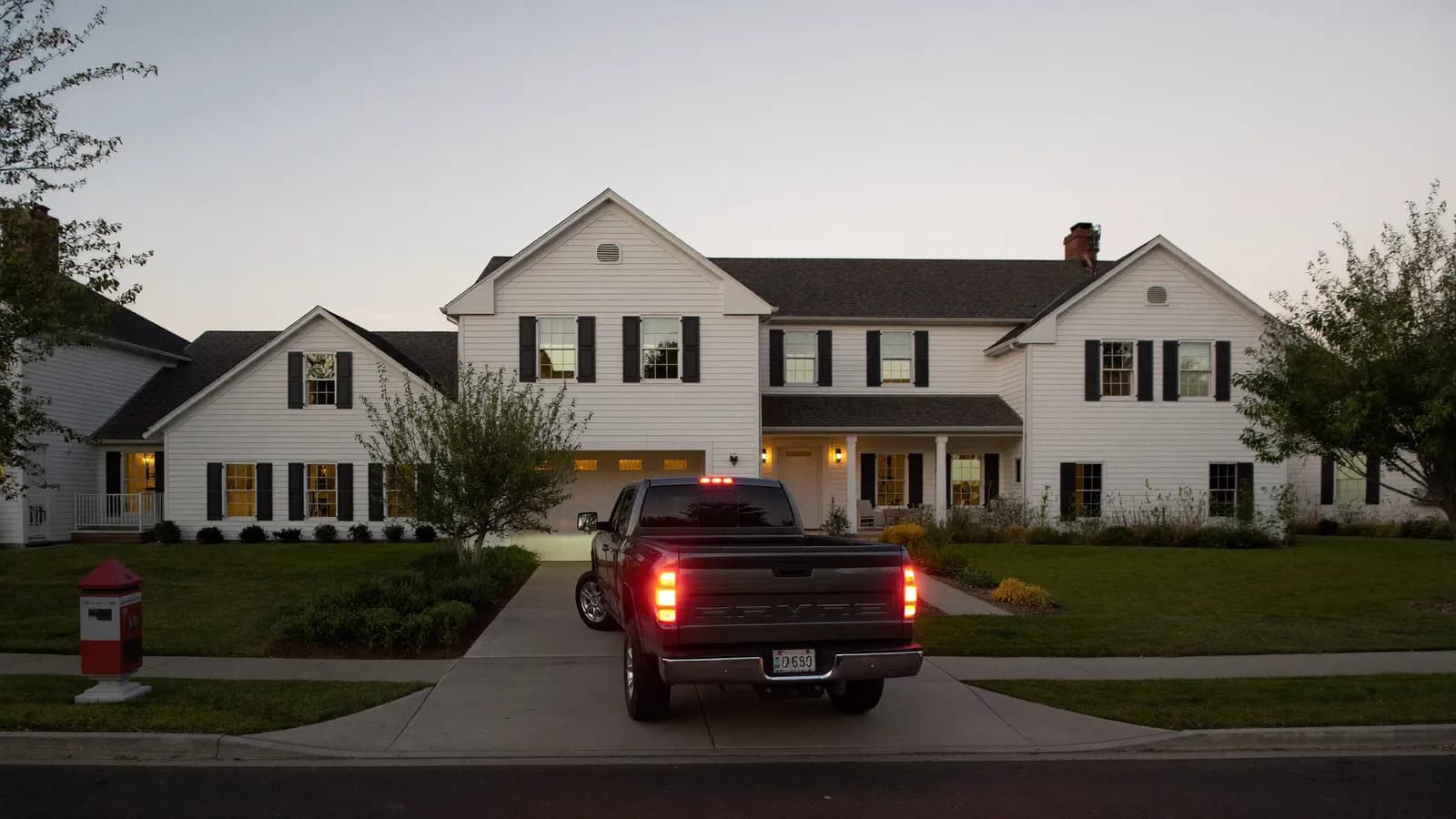A pickup truck pulling into the driveway of a white colonial home at dusk